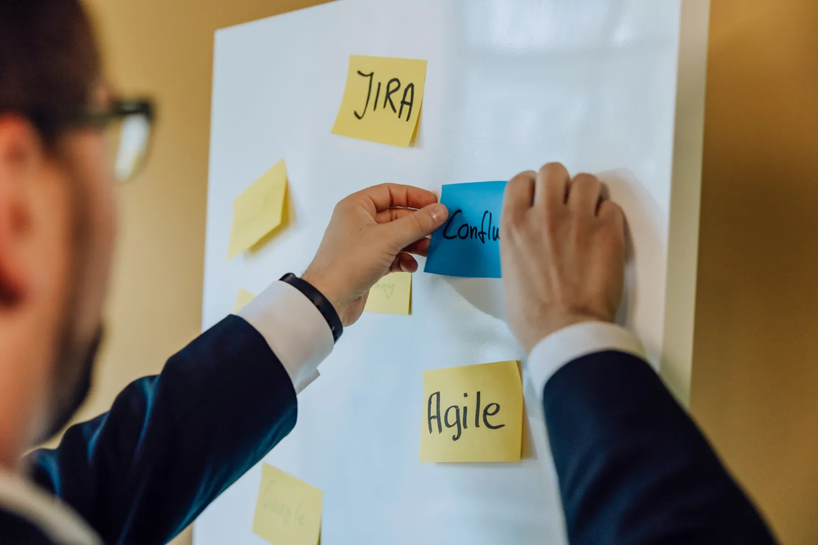 Person placing sticky notes on a whiteboard with words like JIRA and Agile.